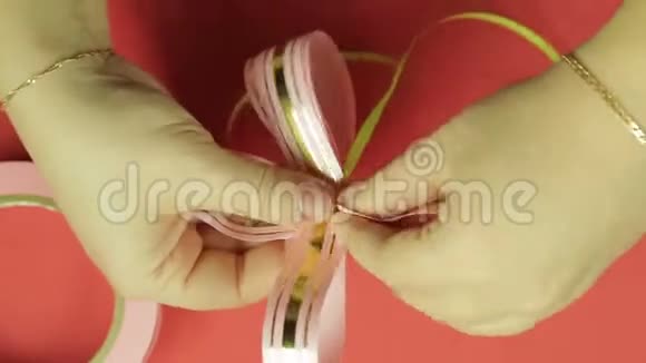 女人手从粉红色丝带上伸直礼物丝带蝴蝶结的花瓣红色背景视频的预览图