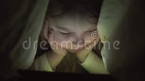 毯子下面有平板电脑的小女孩孩子晚上用药片视频的预览图