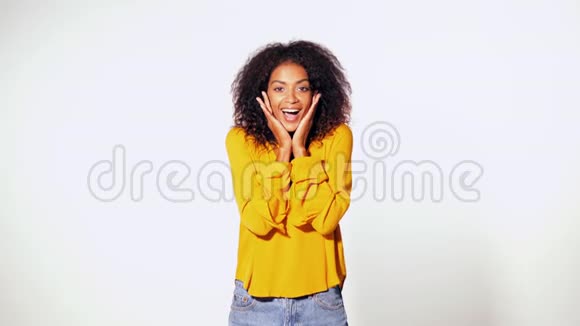 美丽的非洲裔美国妇女头戴黄色非洲头发微笑着惊喜地在白色的墙壁上拍照视频的预览图