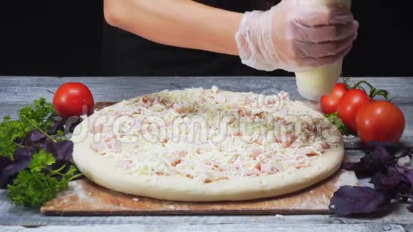 厨师的双手用硅胶手套在木桌上用白酱覆盖比萨饼框架美味可口视频的预览图