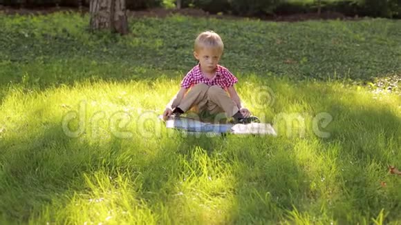 小男孩坐在公园的草地上看相册视频的预览图