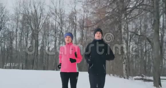 年轻的一家人在冬天的森林里晨跑穿宽松夹克的女人穿黑衣的男人视频的预览图