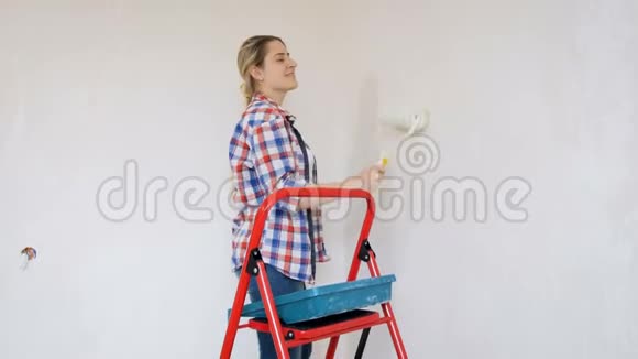一个美丽的年轻女子穿着格子衬衫在她的房子里做装修年轻女孩用油漆粉刷墙壁视频的预览图