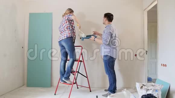 一对幸福的年轻夫妇正在装修他们的新公寓用油漆滚筒粉刷墙壁视频的预览图
