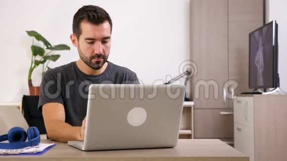 男人在笔记本电脑上微笑和打字然后戴上耳机视频的预览图