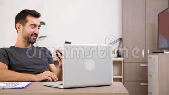 一个男人在客厅的办公桌上通过视频会议用电话交谈视频的预览图