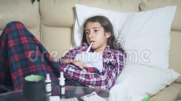 一个十几岁的女孩在家里的沙发上感冒了她用毯子盖住自己测量温度视频的预览图