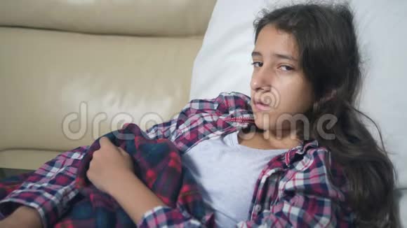 一个十几岁的女孩在家里的沙发上感冒了她用毯子盖住自己测量温度视频的预览图