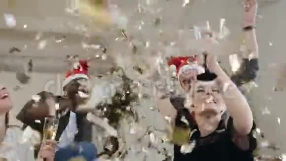 新年快乐的年轻人穿着喜庆的衣服端着酒杯微笑着用飞舞的金色彩纸跳舞视频的预览图