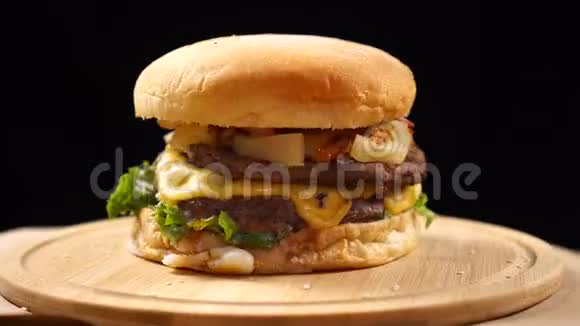 大块多汁的汉堡里面有奶酪酱汁和蔬菜在黑色背景的木板上旋转视频的预览图