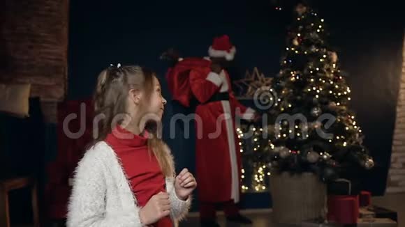 圣诞老人把玩具放在圣诞树上金发小女孩转向圣诞老人视频的预览图