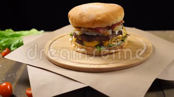 大块多汁的汉堡奶酪酱汁和蔬菜在黑色背景的木板上旋转视频的预览图