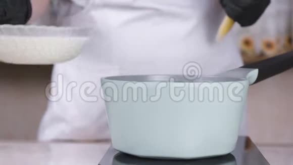 厨师把奶油从碗里倒入平底锅中再加热双手戴黑色手套特写视频的预览图