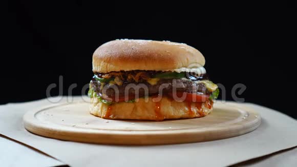 新鲜多汁的汉堡奶酪酱汁和蔬菜在黑色背景的木板上旋转视频的预览图