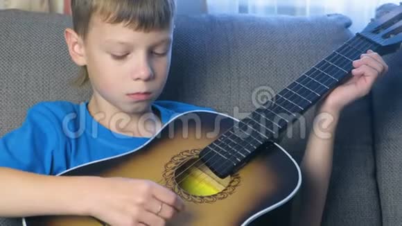 男孩坐在沙发上弹吉他学习演奏乐器的概念视频的预览图