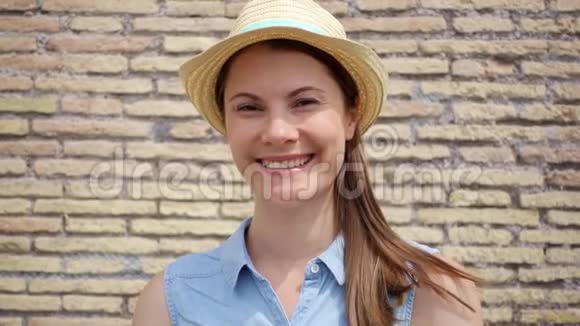戴帽子的女人站在红砖墙上的肖像女性旅行者慢动作微笑视频的预览图