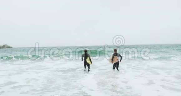 两名男性冲浪者在海滩上与冲浪板一起奔跑的正面景色视频的预览图