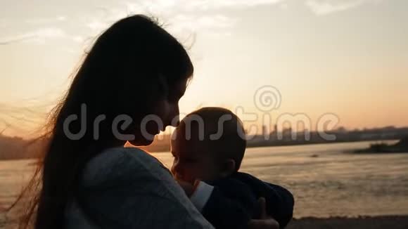 一位年轻的母亲在日落时站在河边时小心翼翼地吻着她的小儿子视频的预览图