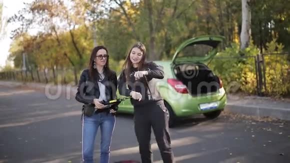 两个女人拿着千斤顶和手在汽车附近跳舞轮子坏了视频的预览图