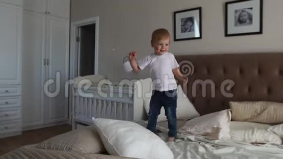 一个穿着白色T恤的男孩跳上床笑着看到父母卧室里有肥皂泡视频的预览图