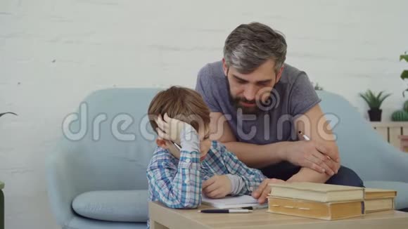 细心的父亲中年留胡子的男人正在帮助他的儿子专心做学校作业孩子在写视频的预览图