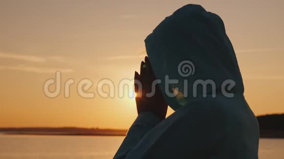 日落时分一个戴着兜帽的中年妇女在湖边祈祷视频的预览图