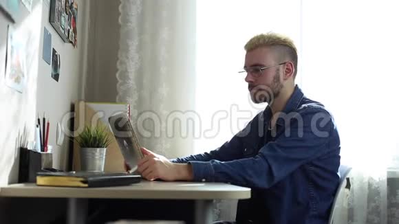 戴着黄色头发眼镜的英俊青年的画像在镜头前显示了拇指家庭自由职业者在家工作视频的预览图