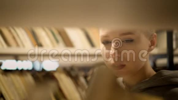 金发女孩在图书馆的书架上挑选一本书视频的预览图