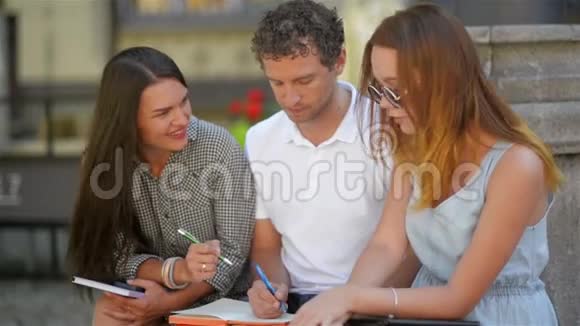 两个漂亮的年轻女孩和一个英俊的男孩与笔记笔和平板准备考试三名学生视频的预览图