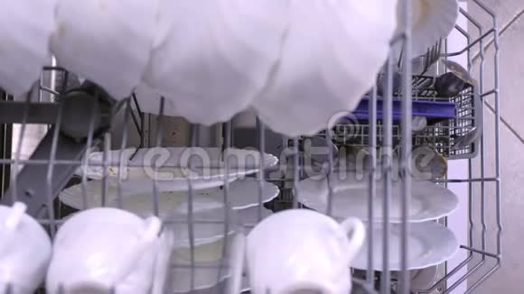 男人在洗碗机里装满脏的白色盘子把篮子推到里面视频的预览图