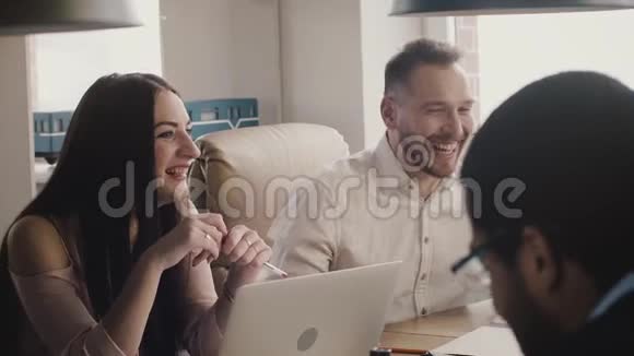 快乐的高加索商人们在同桌慢动作的同事的多民族办公会议上微笑和大笑视频的预览图