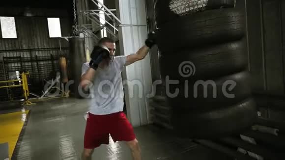 男性好斗的拳击手用汽车轮胎做的拳击袋在拳击中戴着黑拳击手套工作视频的预览图