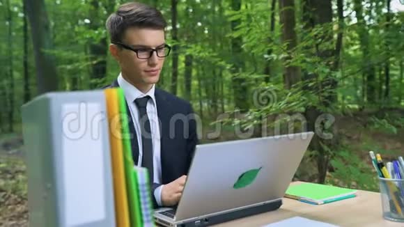 快乐的年轻商人完成他的工作在绿色森林的椅子上放松视频的预览图