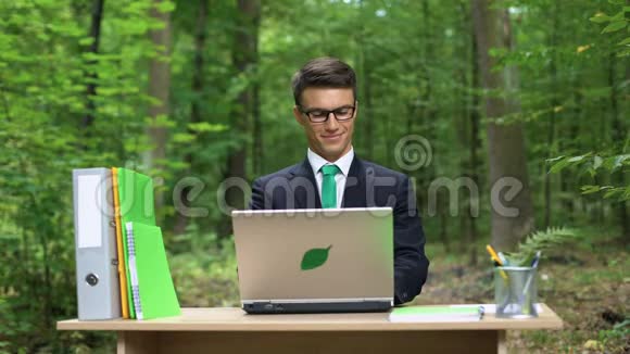一个忙碌的人坐在办公桌上在绿色公园里工作节能笔记本电脑视频的预览图