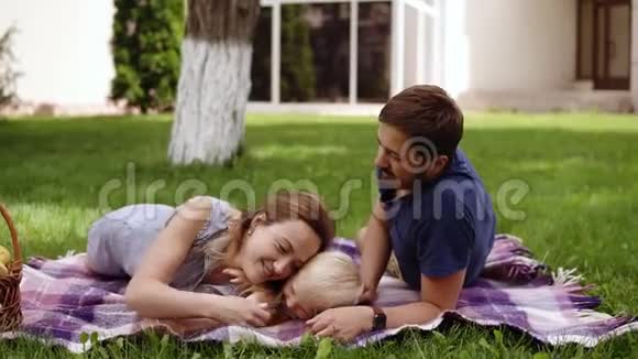 家庭野餐的概念年轻的父母躺在草地上和他的儿子玩玩得开心头发浓密的孩子爬上去视频的预览图