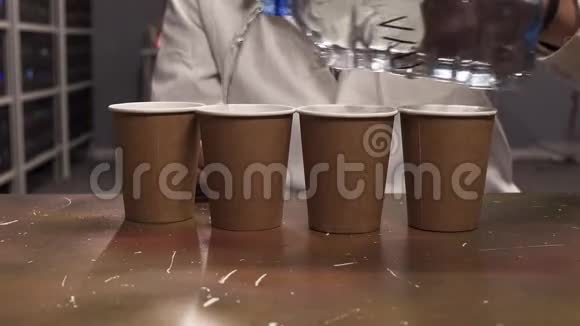 男人他的手在实验室里用白色外套把水从塑料瓶倒到四个纸杯视频的预览图