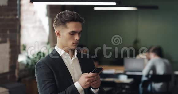 穿西装的年轻商人用智能手机站在现代办公室看着摄像机的人工人视频的预览图
