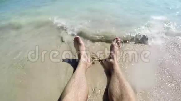 人脚被海浪冲走把它们埋在沙子里一个人的脚躺在沙滩上特写镜头视频的预览图