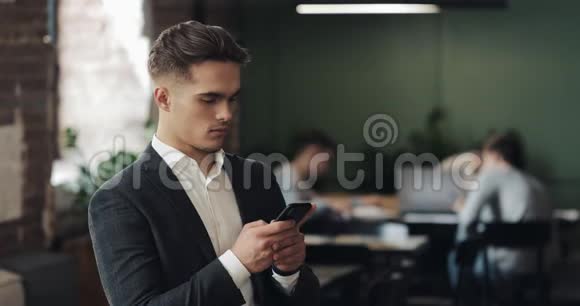 穿西装的年轻商人用智能手机站在现代办公室看着摄像机的人工人视频的预览图