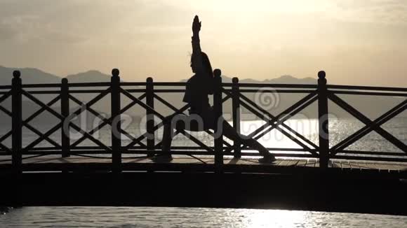 那个女孩在桥上练习瑜伽靠在晨海上动作缓慢视频的预览图