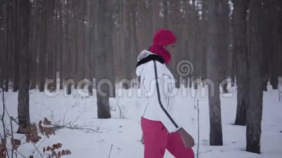 在冬季森林里散步的非裔美国女孩穿着白色保暖夹克的漂亮女孩独自度过时光概念视频的预览图