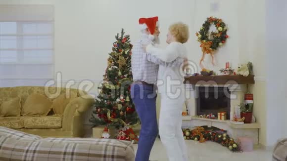 戴着圣诞帽的成年男子和妻子在家中圣诞树附近跳舞视频的预览图