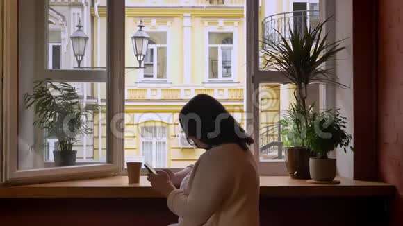 一群穿着纸杯的白种人在靠近窗户的咖啡馆里用手机滚动着视频的预览图