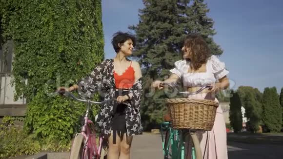 两个穿着鲜艳衣服的积极的女人在街上狭窄的路上牵着自行车说话农村生活视频的预览图