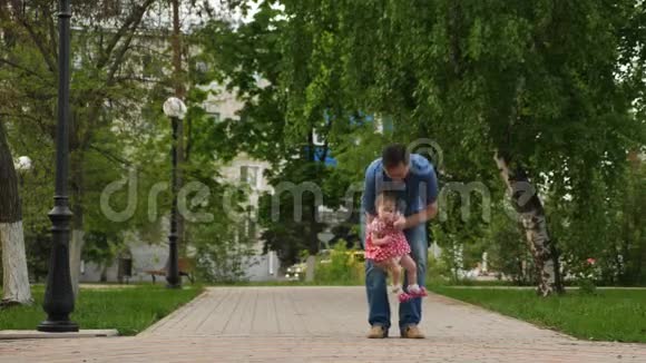 快乐的宝宝在做他的第一步让爸爸的手在绿色公园散步在白天视频的预览图