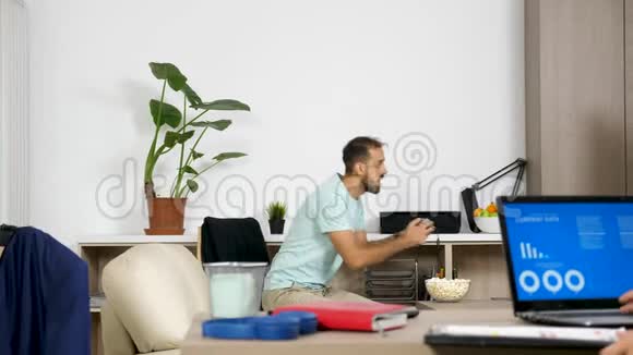 男人在控制台上玩电子游戏而她的伴侣正在电脑上工作视频的预览图