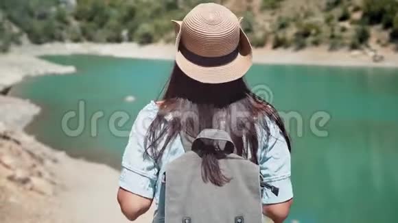 后景活动徒步旅行者女游客帽子和太阳镜从山到池塘下降视频的预览图