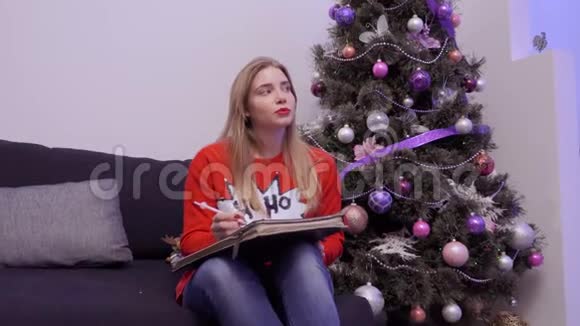 穿红色毛衣的年轻女孩在圣诞节时写购物清单视频的预览图