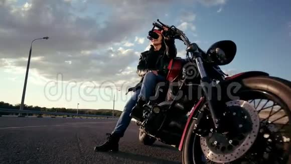 穿着皮夹克和手套坐在摩托车上的老妇人骑自行车背景有一条空公路视频的预览图