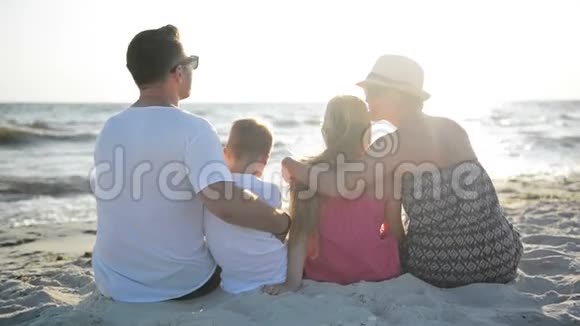 可爱的家庭拥抱坐在海边的沙滩上看着太阳和波浪视频的预览图